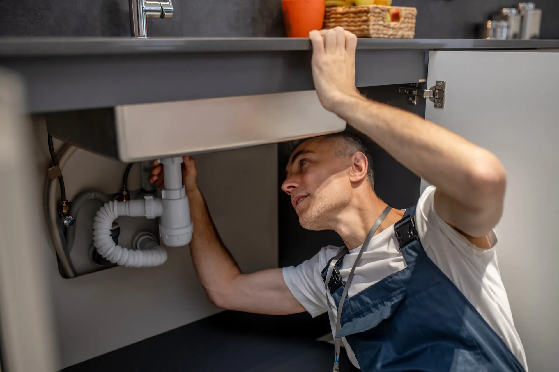 Plumber examining pipes under a kitchen sink